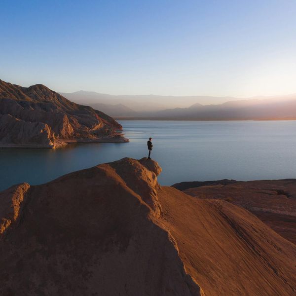 Person meditating peacefully by a calm lake at sunrise.